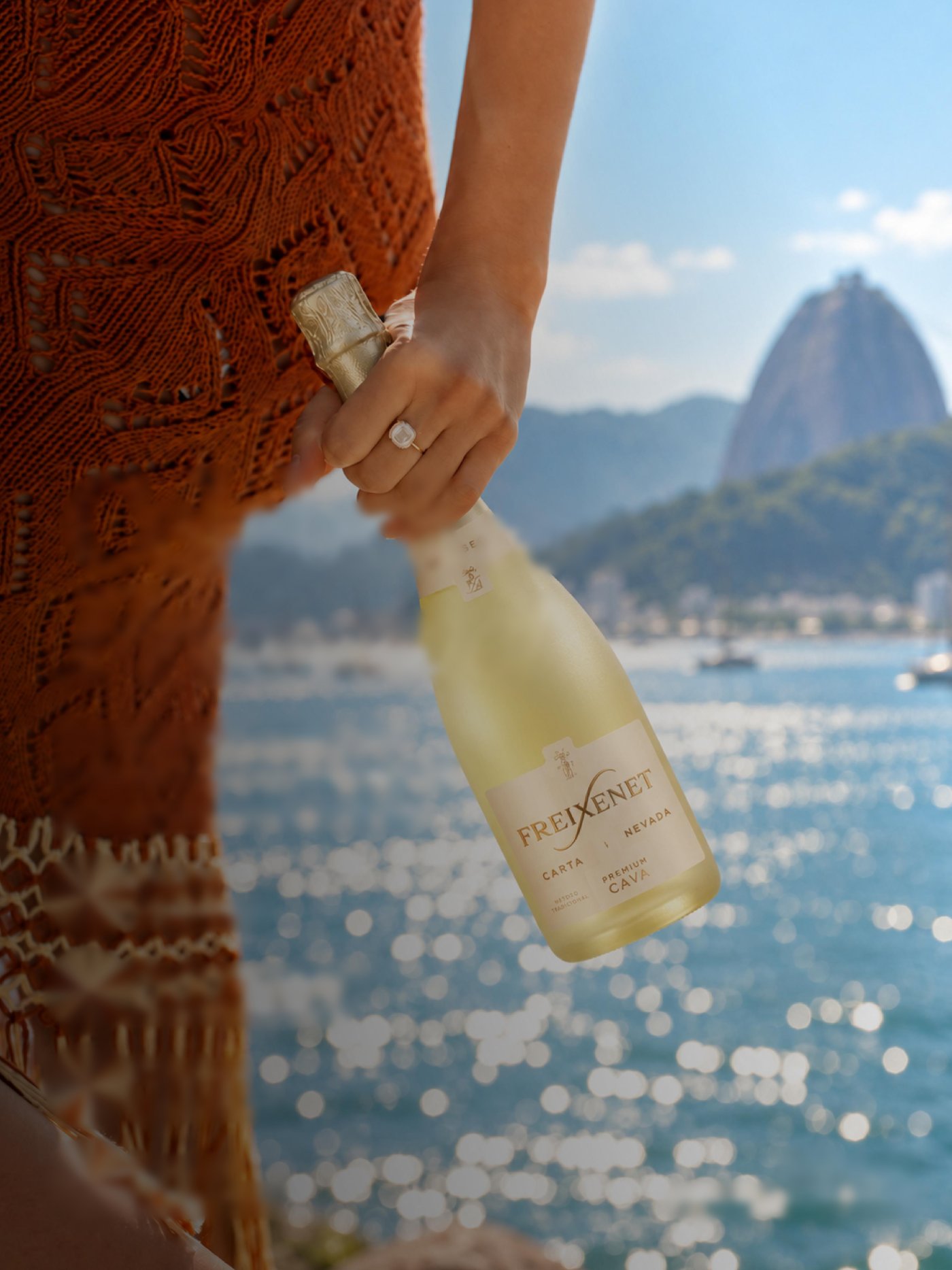Mano sosteniendo una botella de Freixenet Carta Nevada frente a la bahía de Río de Janeiro